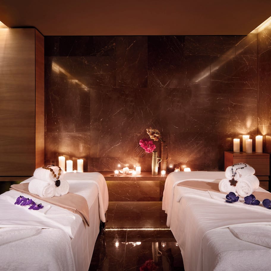 A spa room with two beds, candles, and a vase with flowers.