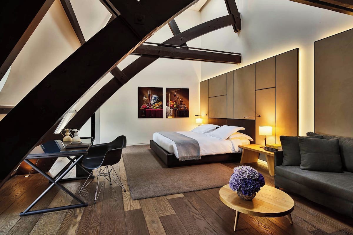 A modern loft bedroom with a bed, a sofa, a small table, and a desk with a chair.