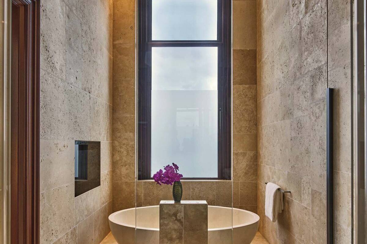 Ein modernes Badezimmer mit einer großen, ovalen Badewanne, einem Fenster mit Milchglas und einer Vase mit violetten Blumen.