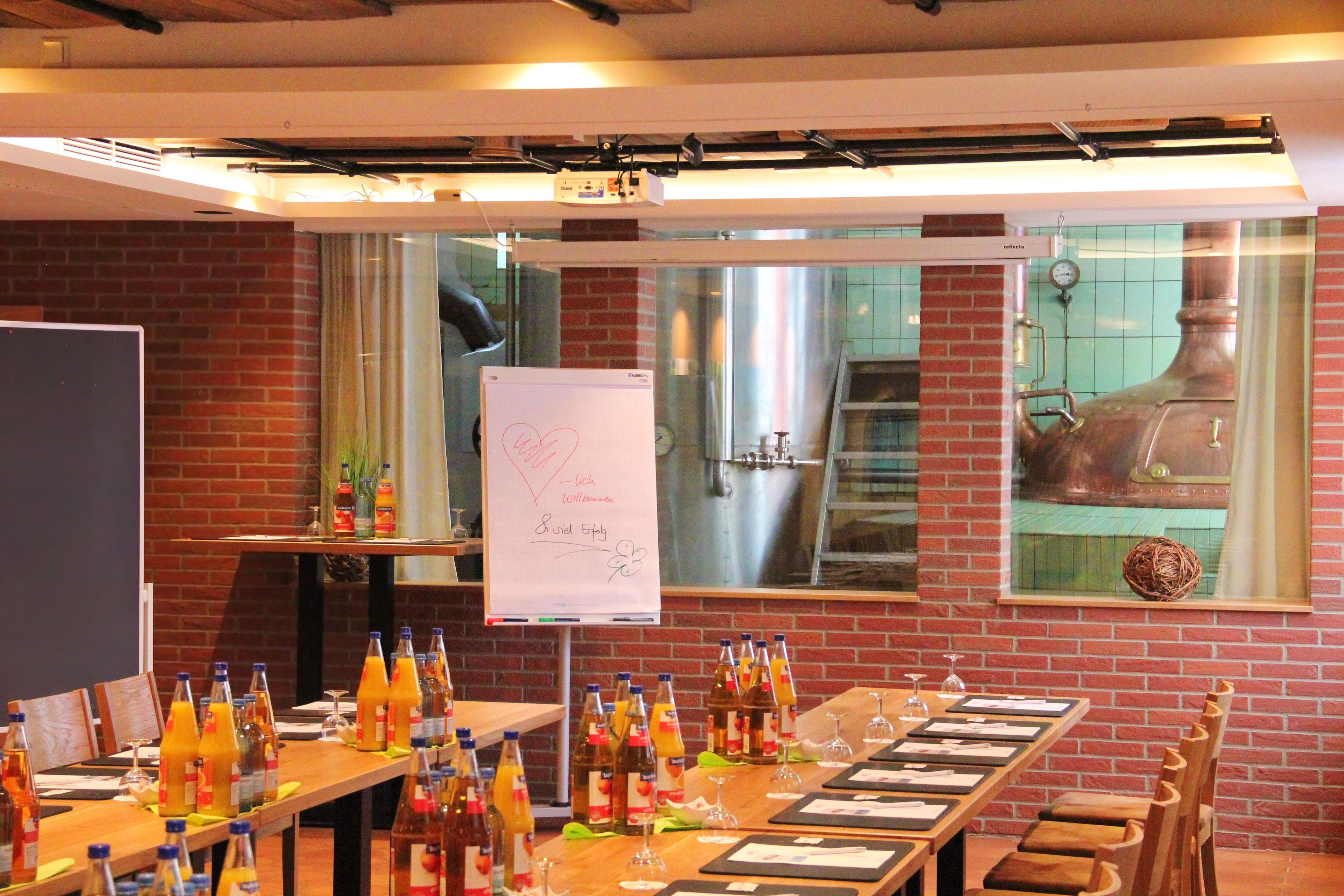 A conference room with a long table set for a meeting, a whiteboard with handwritten notes, and a brick wall with a large industrial oven.