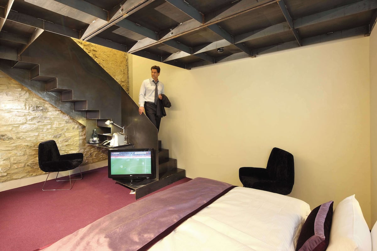 Une chambre d’hôtel avec un lit, un bureau équipé d’un ordinateur, une chaise, une télévision et un escalier.