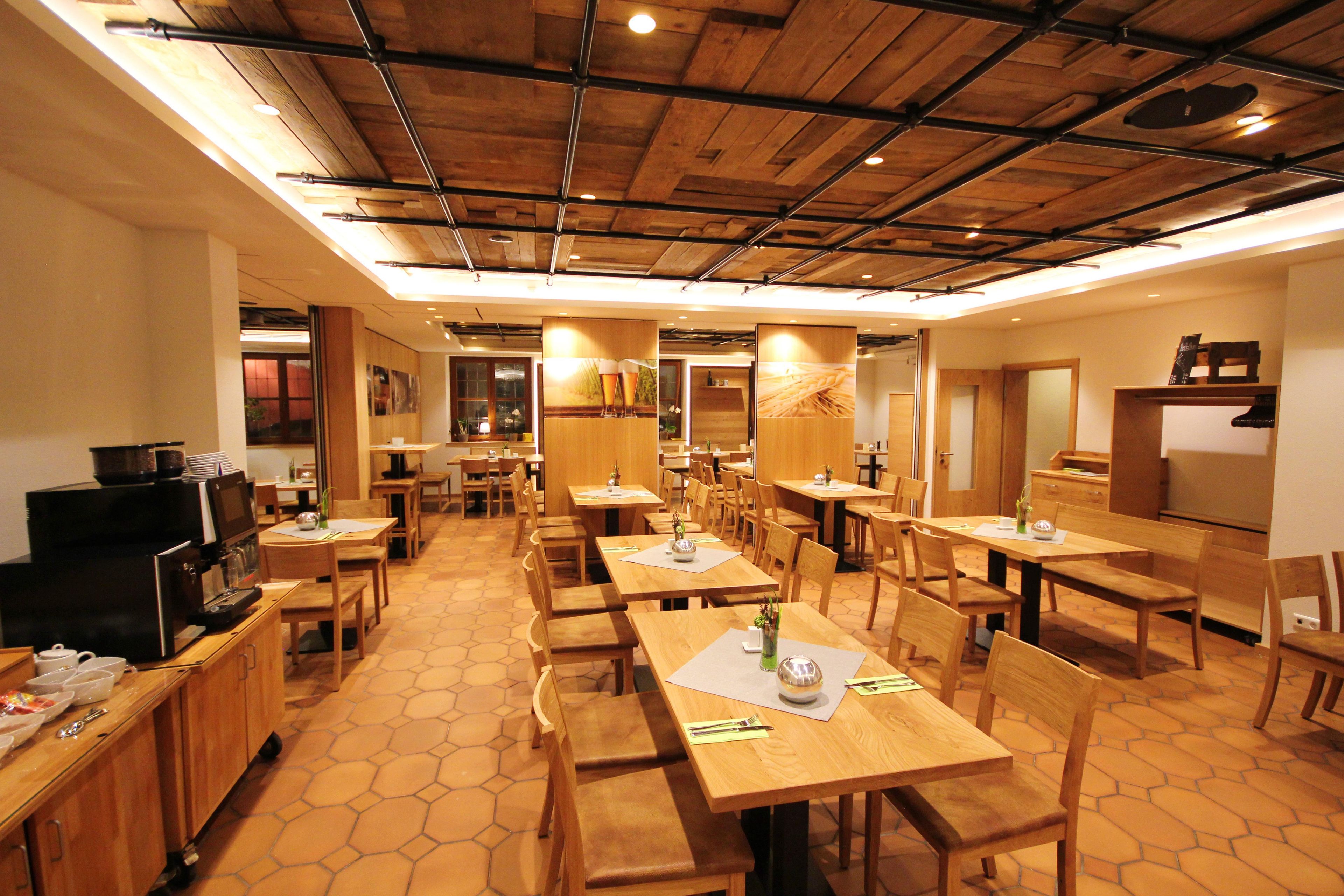 Un restaurant avec des tables et des chaises en bois, un espace cuisine et un plafond avec des poutres apparentes.