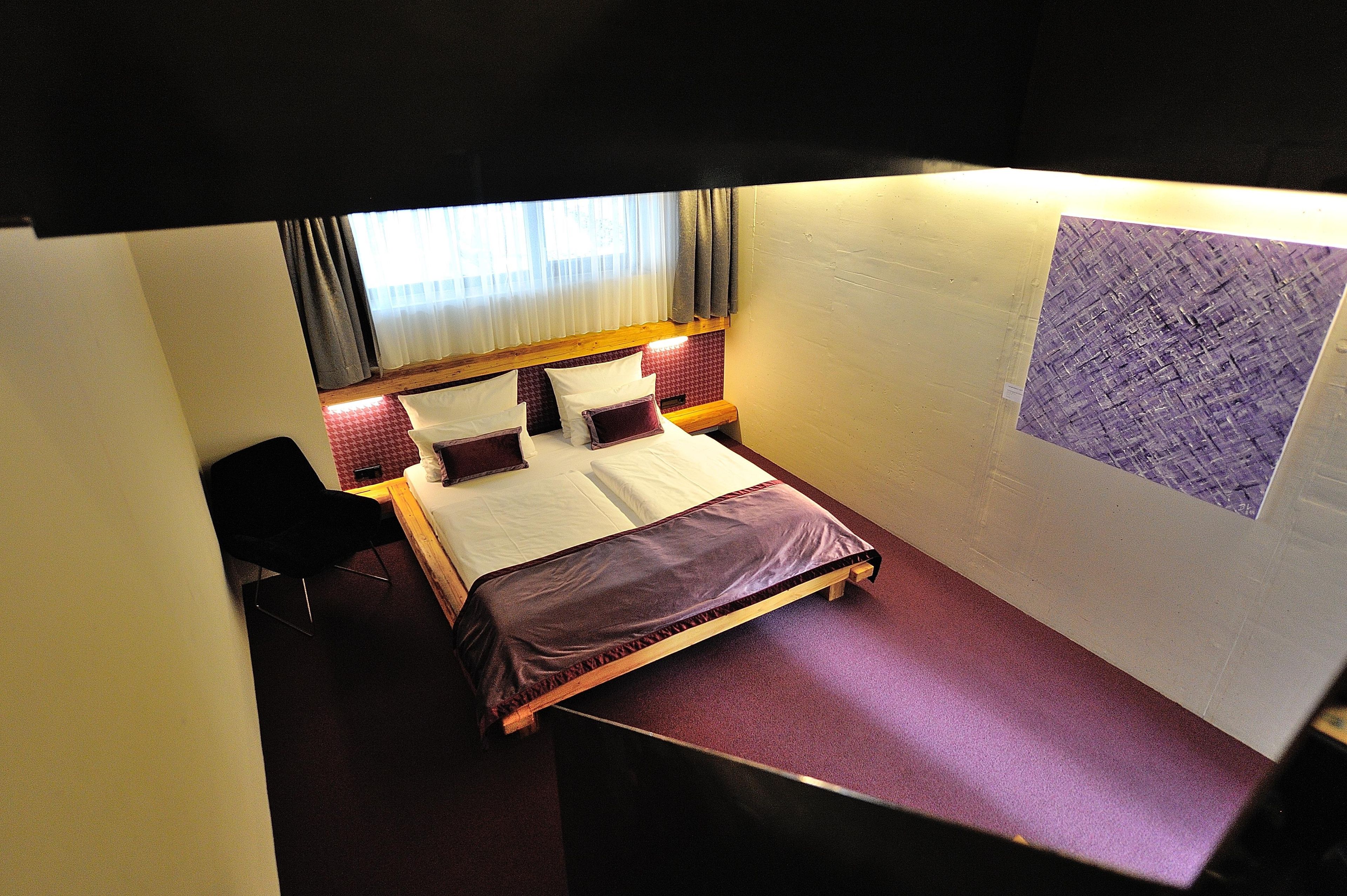 Un dormitorio pequeño y funcional con una cama individual, una silla y un ventanal con cortinas.