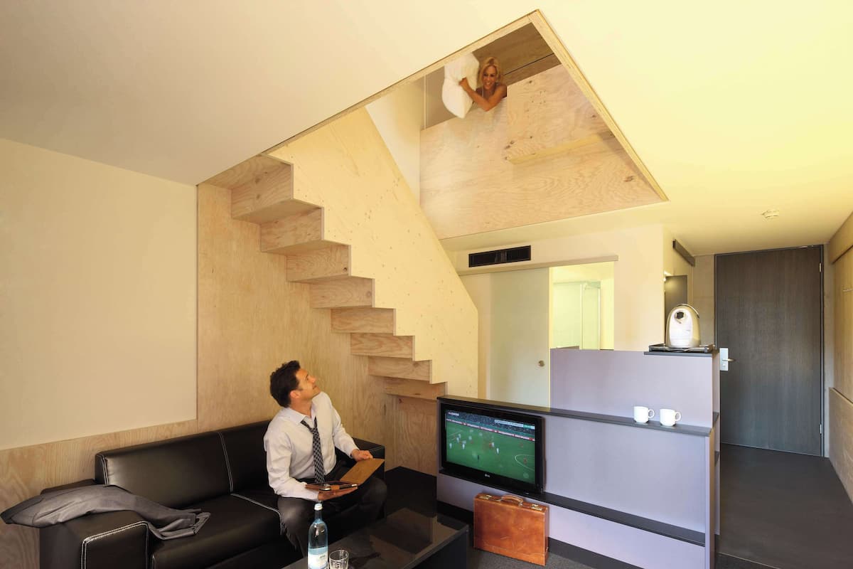 Un salon moderne avec un canapé en cuir noir, un téléviseur à écran plat et un escalier en bois.