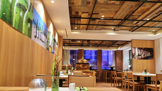 Een restaurantinterieur met houten balkenplafond, een eetgedeelte met tafels en stoelen, en een muur met ingelijste foto's.