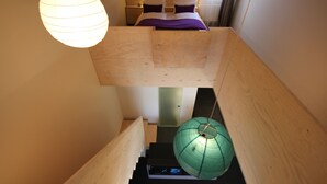 Een moderne hotelkamer met een houten stapelbed, een groene hanglamp en een digitale klok op het nachtkastje.