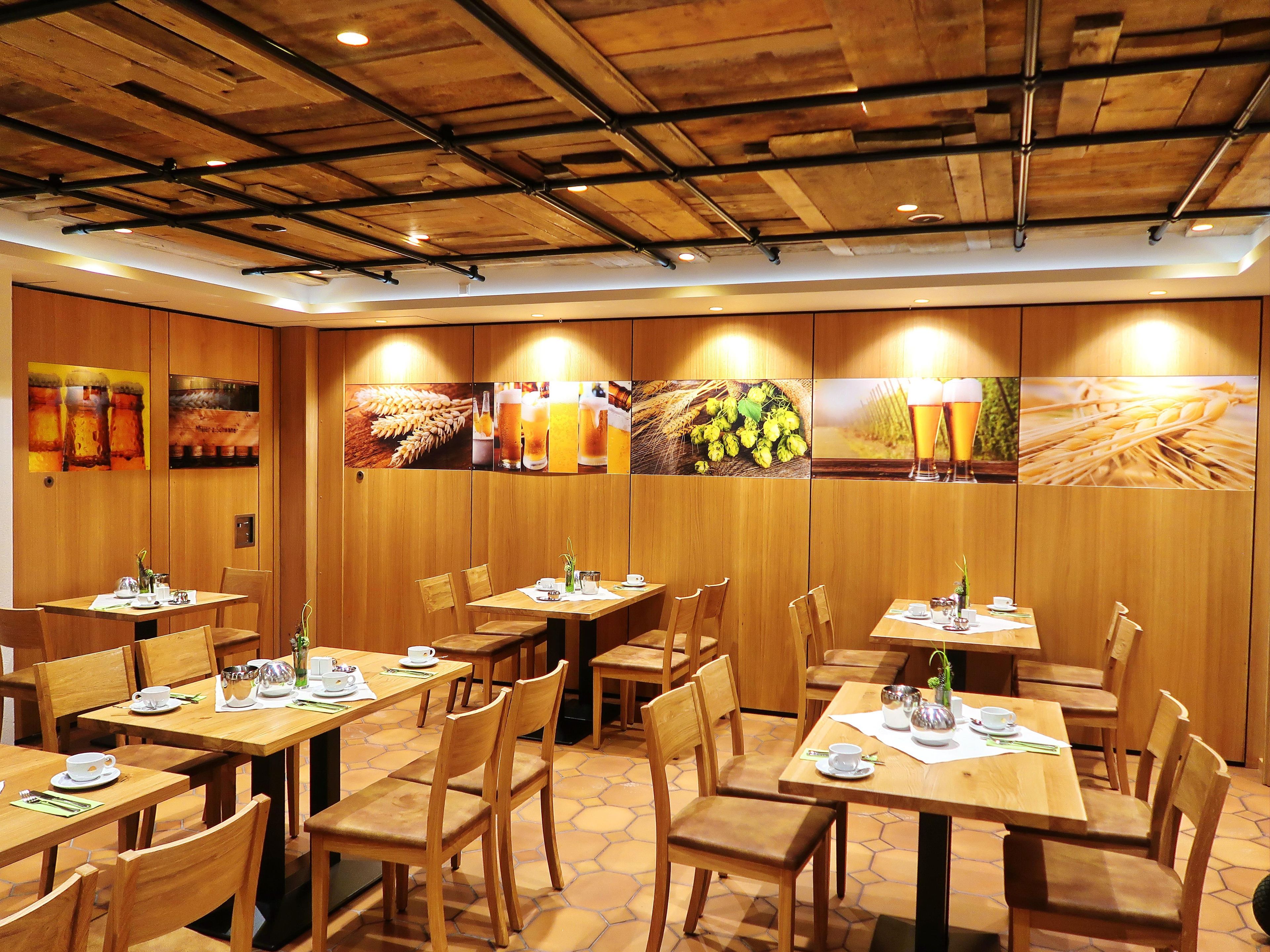 A restaurant with wooden tables and chairs, a tiled floor, and wall art depicting food and drink.