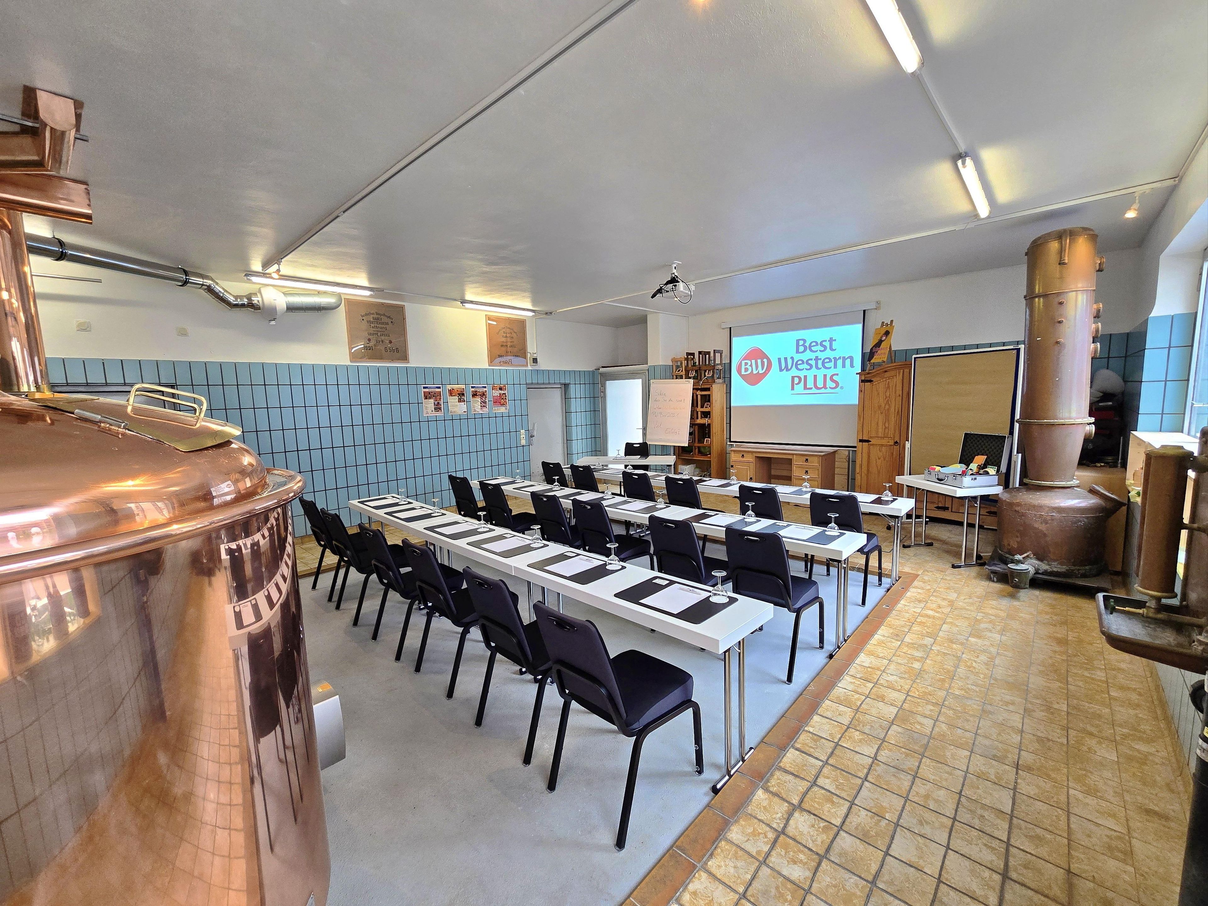 A conference room with a long table, chairs, a projector screen, and a large copper vessel.
