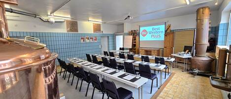 A conference room with a long table, chairs, a projector screen, and a large copper vessel.
