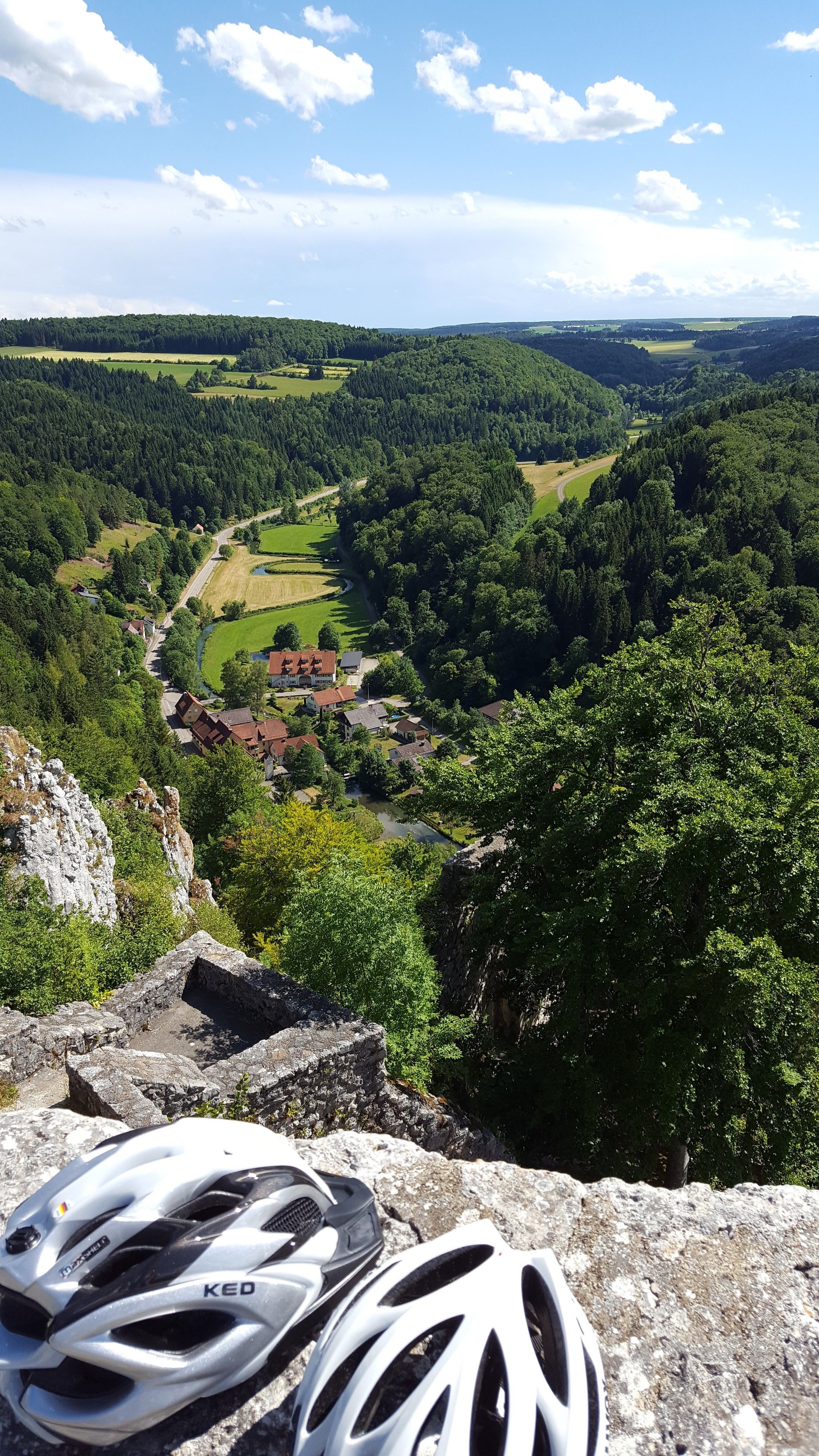 A mountain landscape with a village, a road, and a bicycle helmet on a rock.