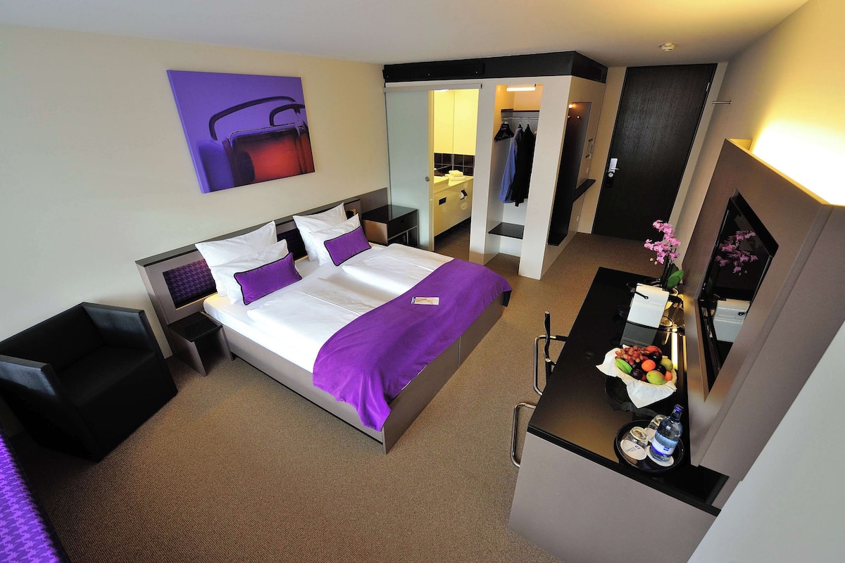 Une chambre d’hôtel moderne, dotée d’un grand lit, d’un bureau et d’une salle de bain visible à travers une porte ouverte.