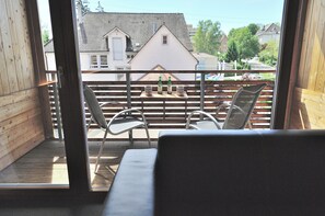 A balcony with a wooden floor, metal railing, and two metal chairs.