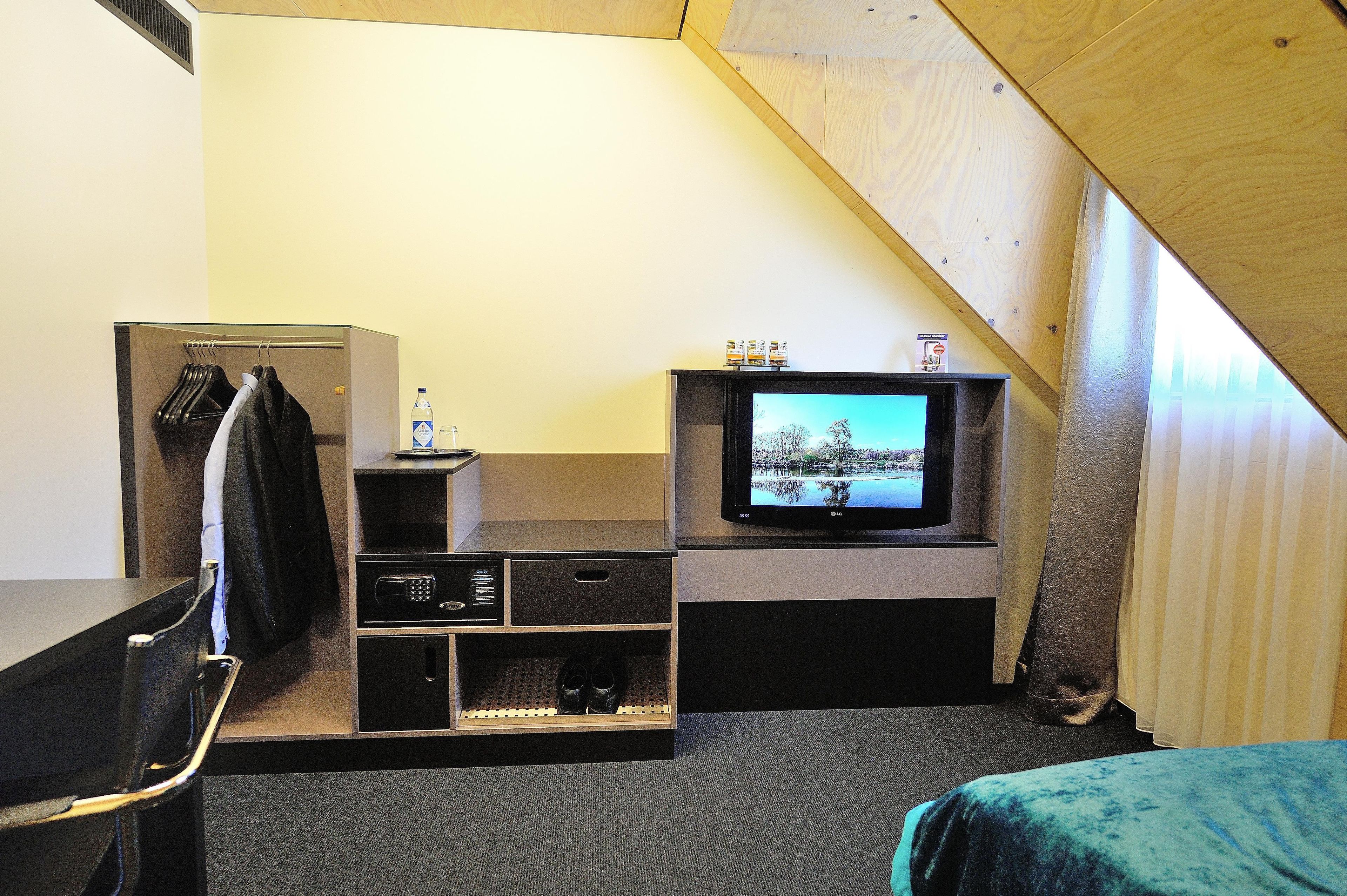 A small room with a television on a stand, a coat rack, and a shoe rack.