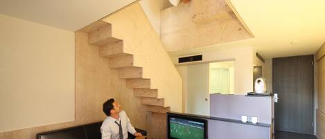 A modern living room with a black leather sofa, a flat-screen TV, and a wooden staircase.