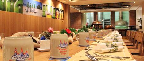 Restaurante com mesas compridas preparadas para refeições, com um tradicional copo de cerveja bávaro como peça central.
