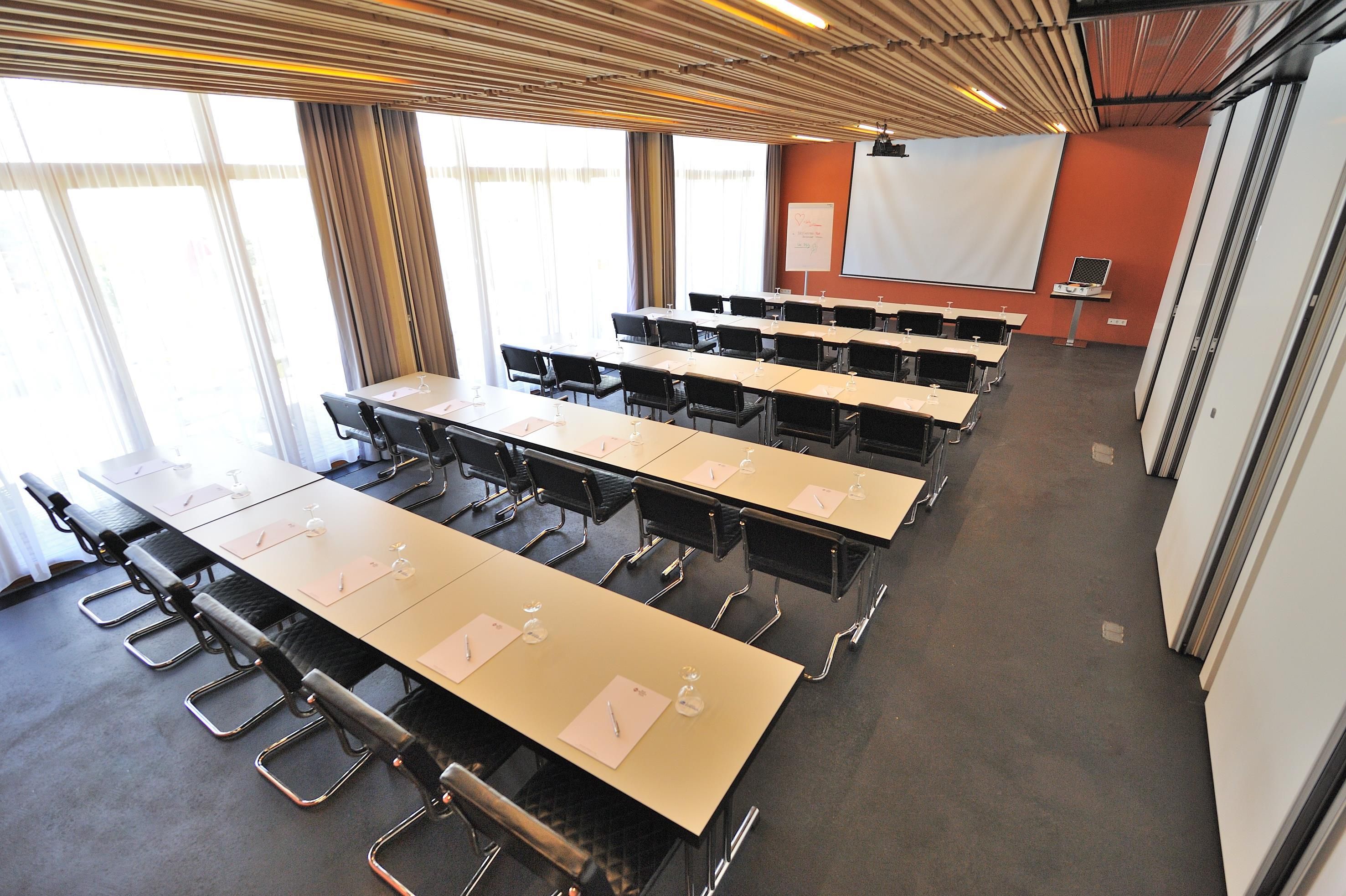 A conference room with multiple tables and chairs, a projector screen, and a whiteboard.