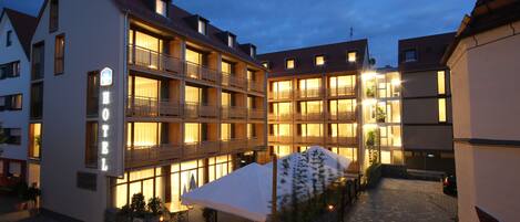 A hotel with multiple balconies, a covered outdoor seating area, and a paved courtyard.
