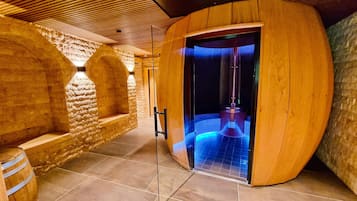 Ein Wellnessraum mit einem Holzfass, Steinwänden und einer blau beleuchteten Wasserspülung.