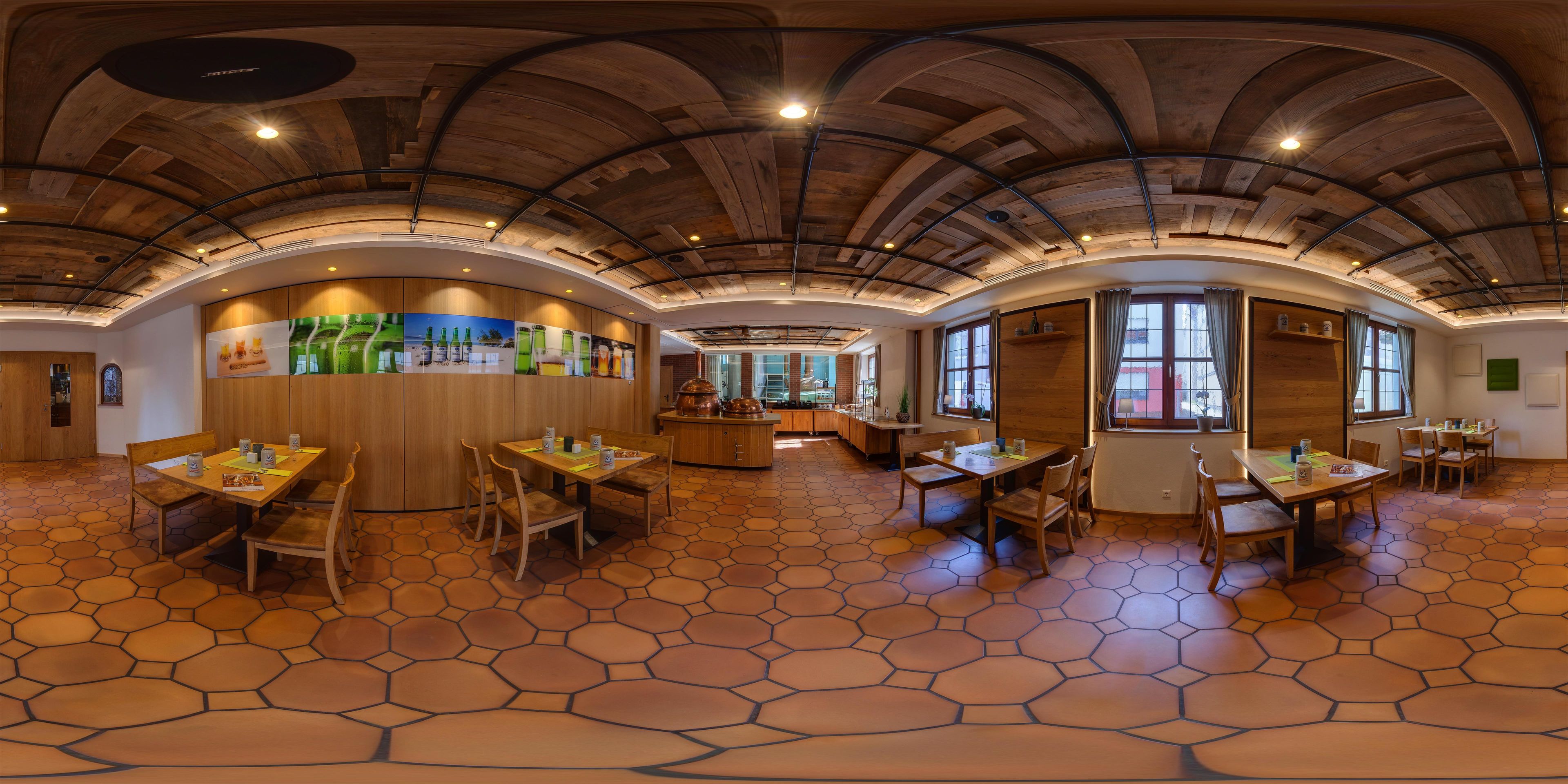 Un restaurante con suelo de baldosas hexagonales, mesas y sillas de madera, una zona de bar central y un techo curvo con vigas a la vista.