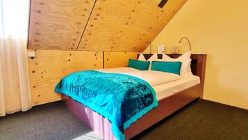 Ein Schlafzimmer mit Holzbalkendecke, einem Bett mit türkisfarbener und weißer Bettwäsche und einem Nachttisch mit Lampe.