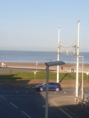 En kustväg med en blå bil parkerad vid sidan om, en gångbana och en strand i bakgrunden.