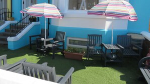 A patio area with two striped umbrellas, outdoor seating, and a view of the Eiffel Tower through a window. - Waters Edge (Blackpool)
