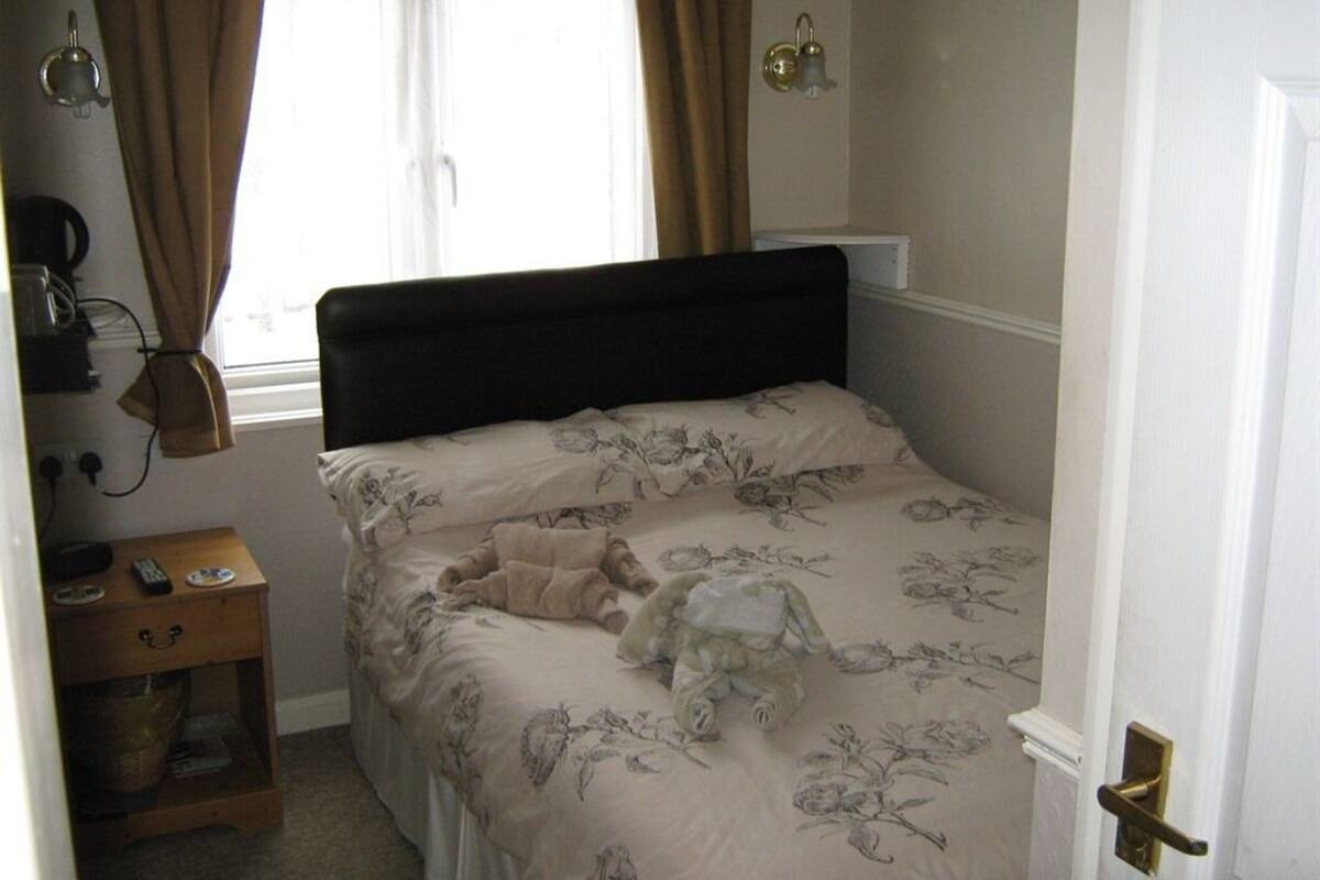 Une chambre à coucher avec un lit, une table de chevet, une lampe et une fenêtre avec des rideaux.