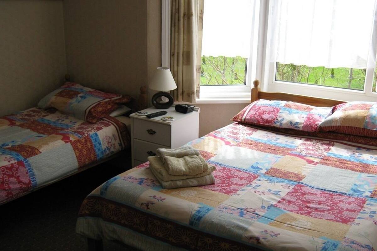Une chambre avec deux lits simples, une table de chevet avec une lampe et une fenêtre avec des rideaux.