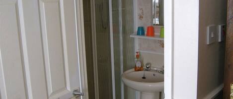 A bathroom with a white door, a shower, a sink, and a mirror.