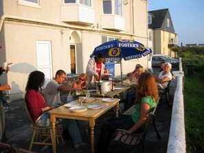 A group of people dining outdoors at a table with a Foster's branded umbrella.