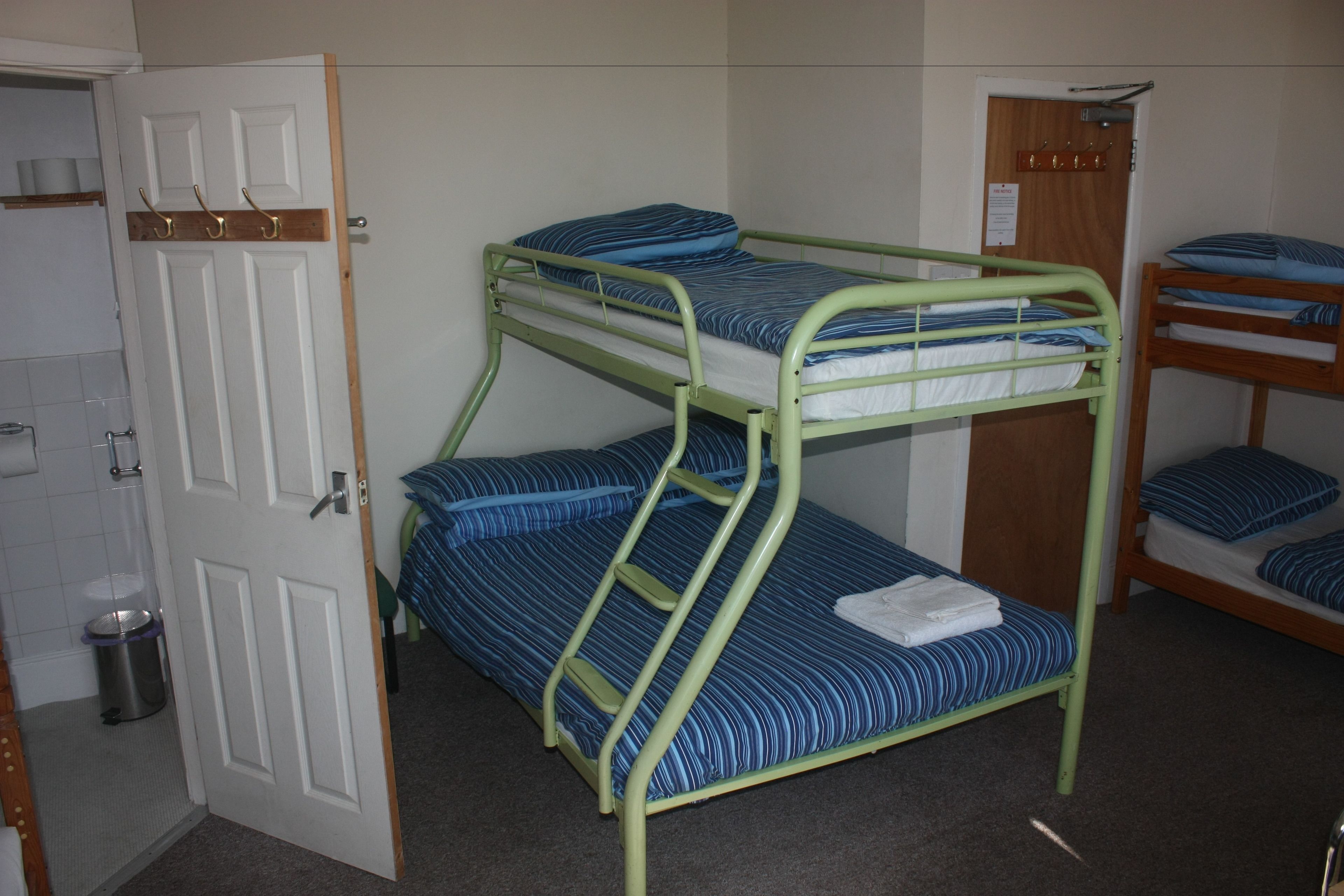 A bunk bed room with a door, a trash bin, and a wooden door frame.