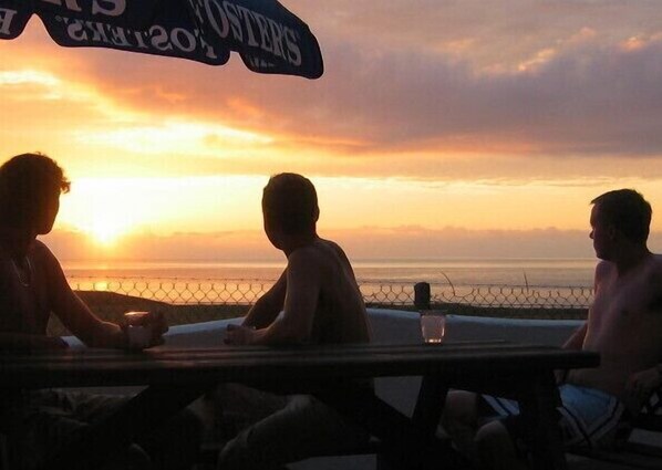 Three people sitting at a table with a view of the sunset over the ocean.