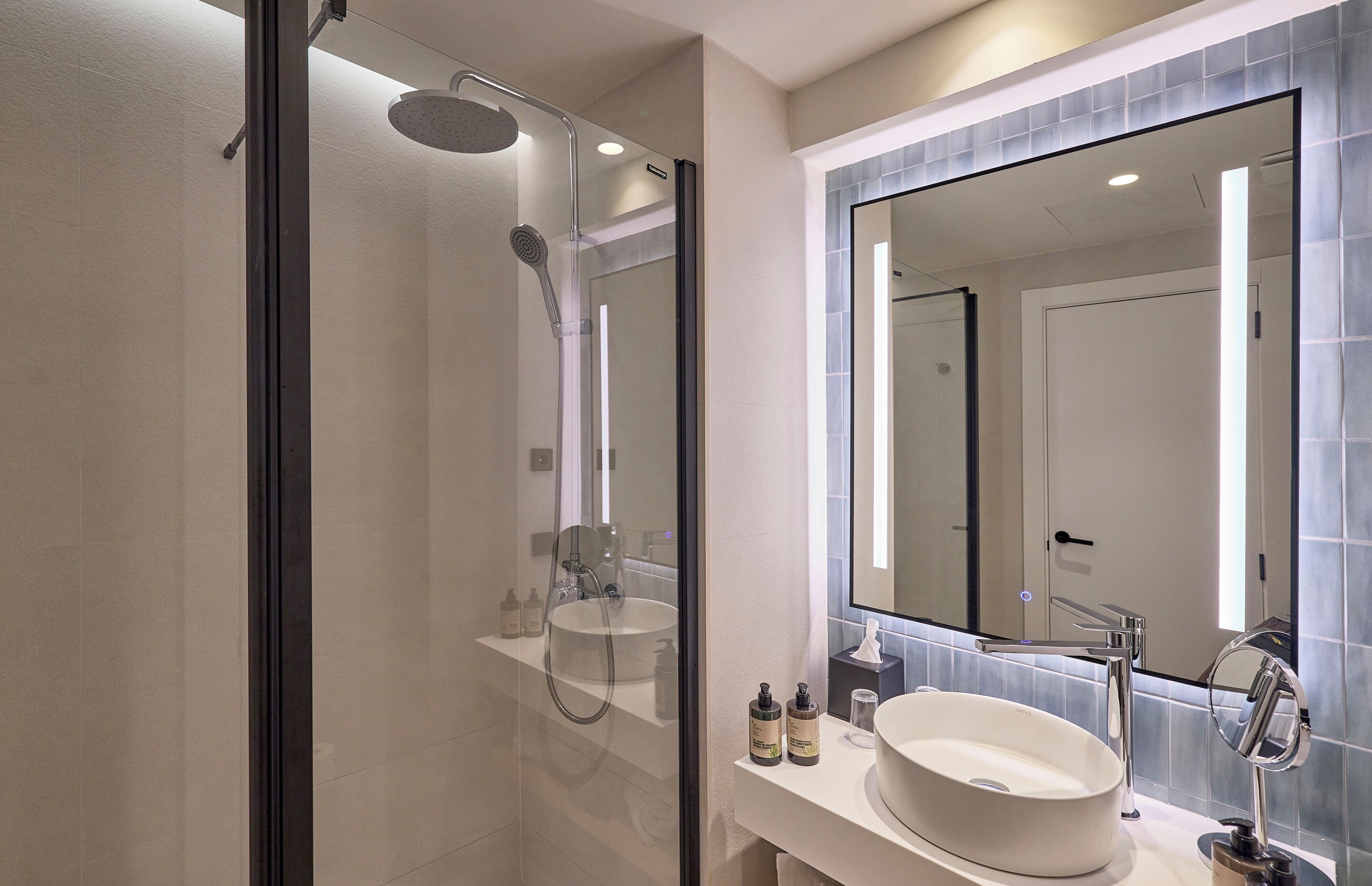 A modern bathroom with a glass-enclosed shower, a large mirror, and a white sink.