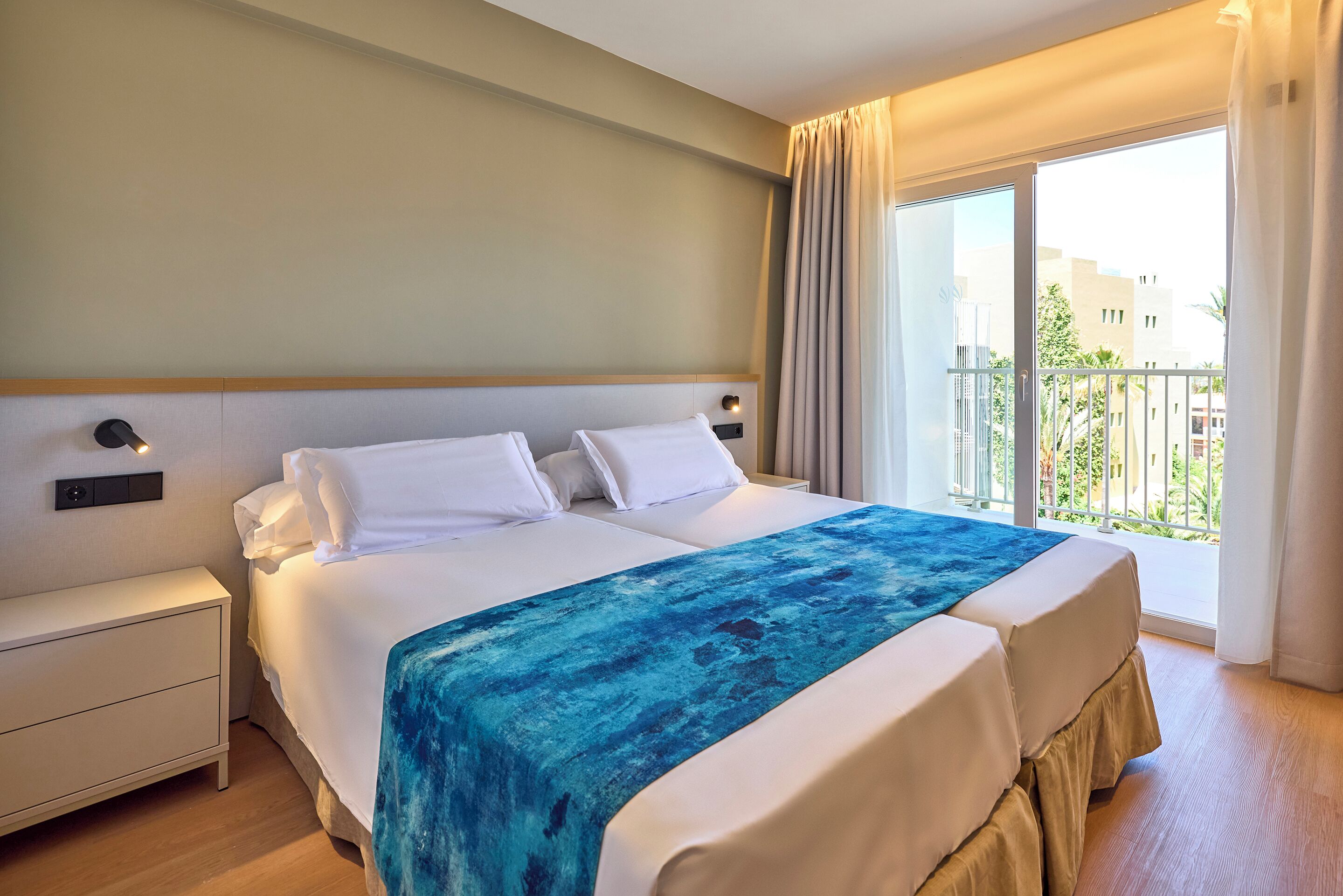 A hotel room with a large bed, a nightstand, and a view of the outdoors through a balcony.