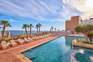 Zona de piscina con sillones de descanso y sombrillas, una piscina cristalina y vistas al mar.