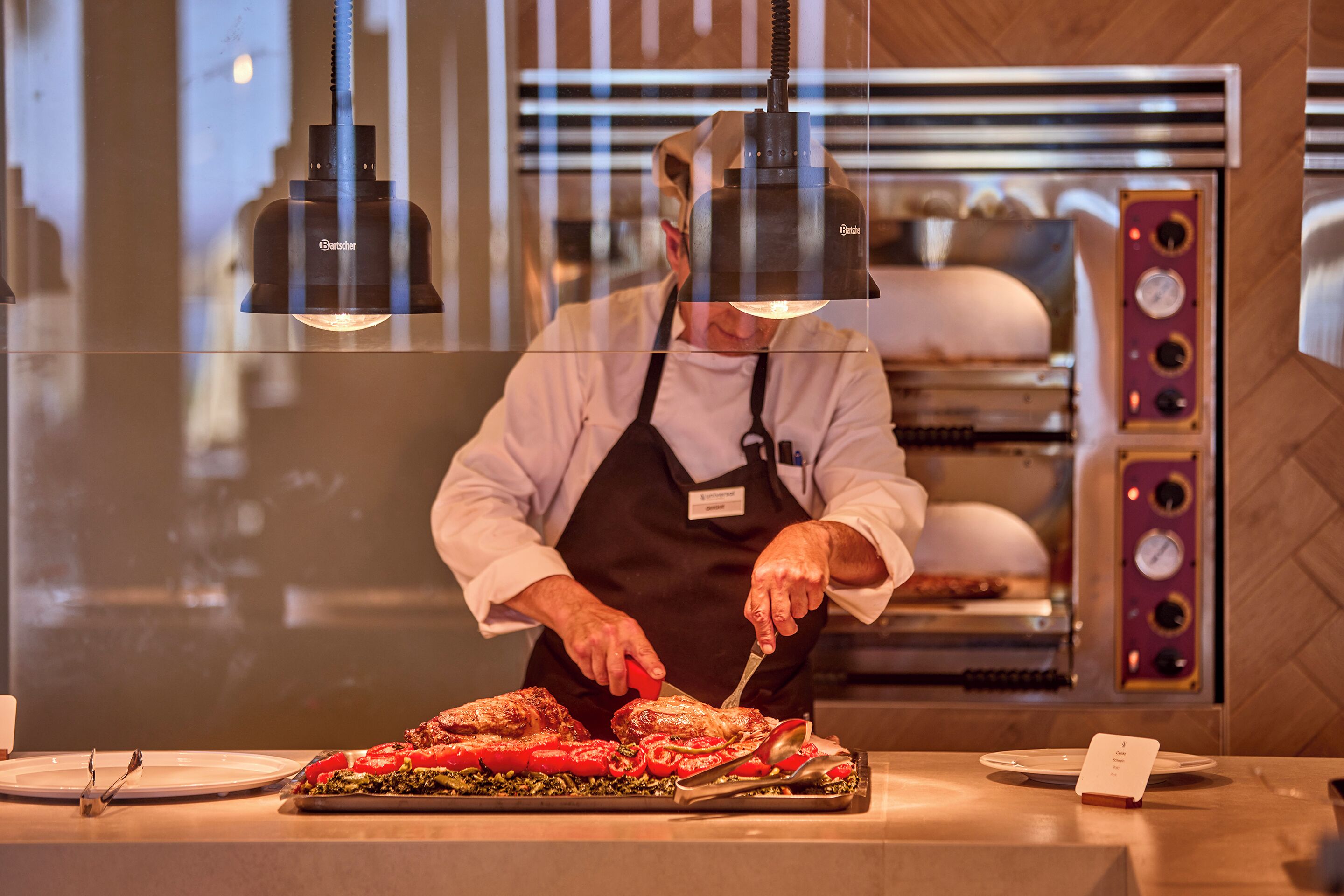 A chef slicing meat at a counter with a commercial oven in the background.
