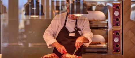 A chef slicing meat at a counter with a commercial oven in the background.