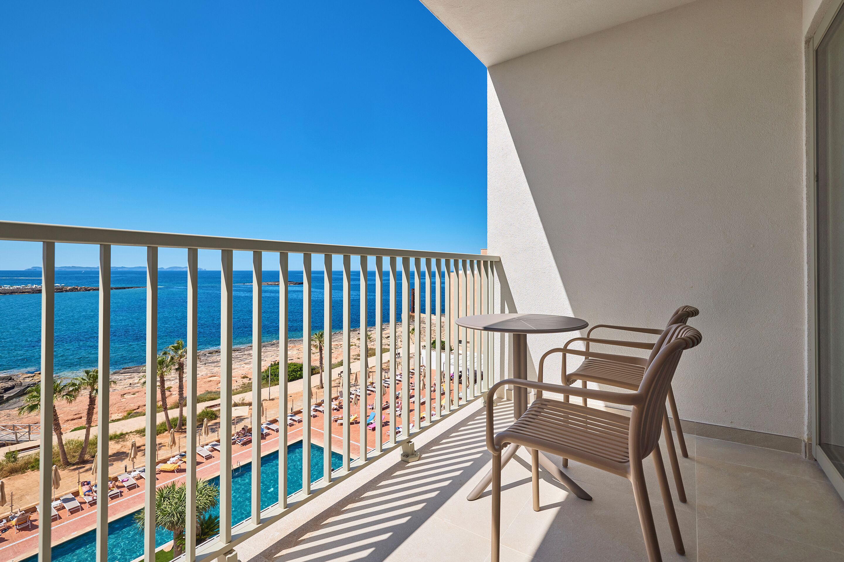 Ein Balkon mit Blick auf Strand und Pool, ausgestattet mit zwei Stühlen und einem Tisch.