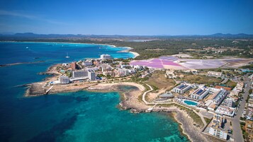 Vista aérea de un complejo turístico costero con varios edificios, una playa y una gran piscina.