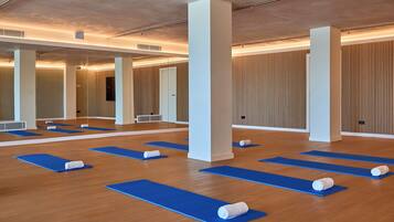 A spacious room with wooden floors, blue yoga mats, and white pillars.