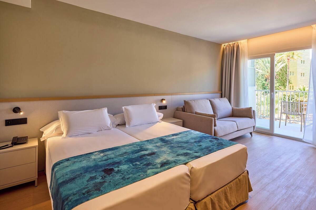Quarto de hotel com uma cama grande, um sofá, uma mesa de cabeceira e vista para o exterior.