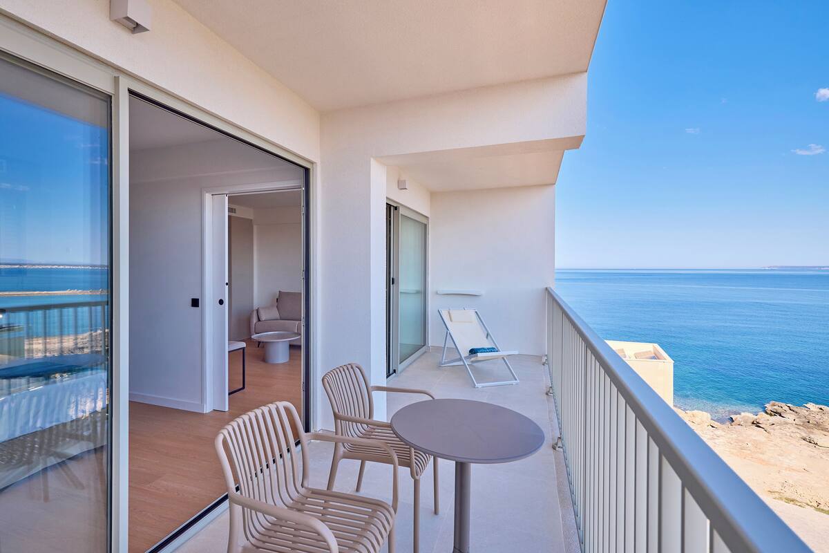 Uma varanda com mesa, cadeiras e uma poltrona, com vista para o mar.