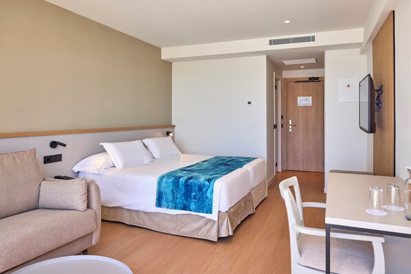 A hotel room with a bed, a sofa, a table with glasses, and a TV on the wall. - Universal Hotel Romantica (Ses Salines)