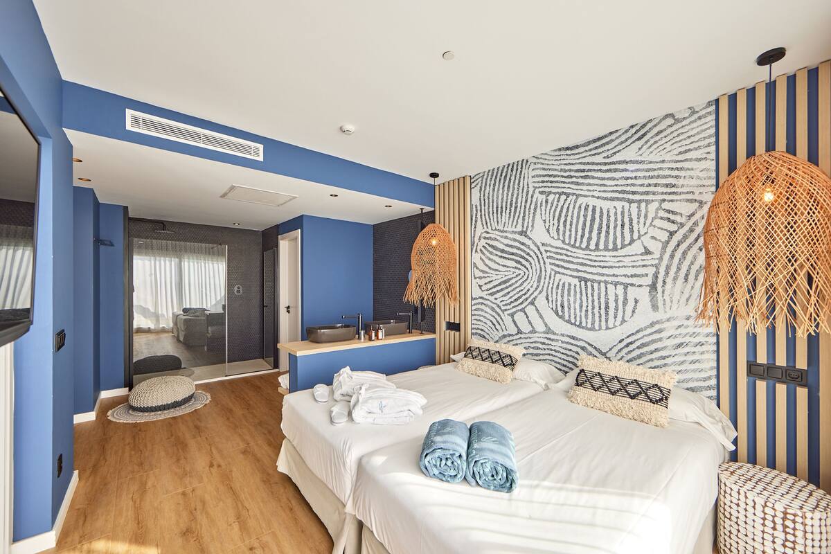 Une chambre d’hôtel moderne dotée d’un grand lit, d’une salle de bain avec un grand miroir et offrant une vue sur la ville.