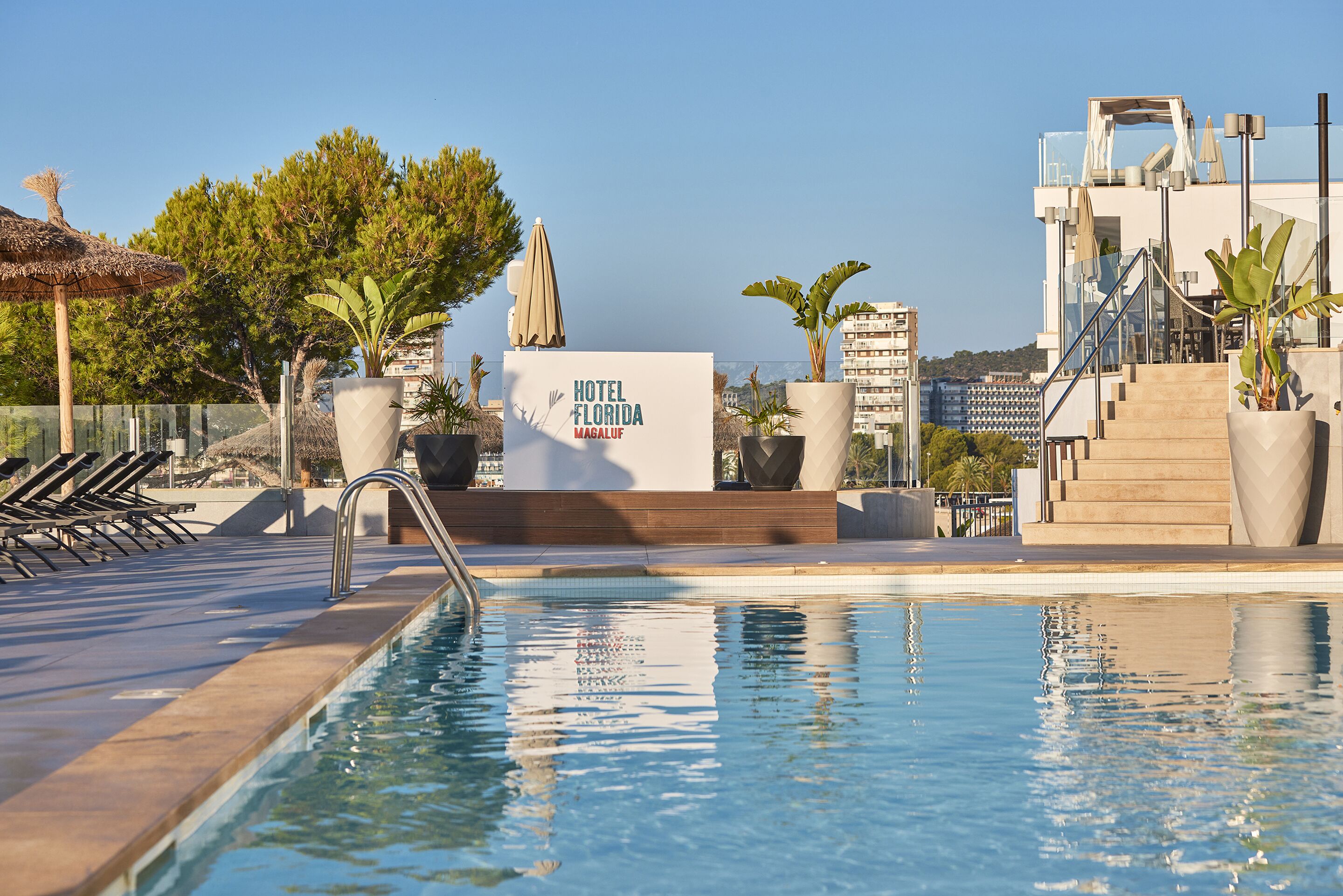 Una piscina con sillas de descanso, un cartel de Hotel Florida Magalu y vistas de la ciudad.