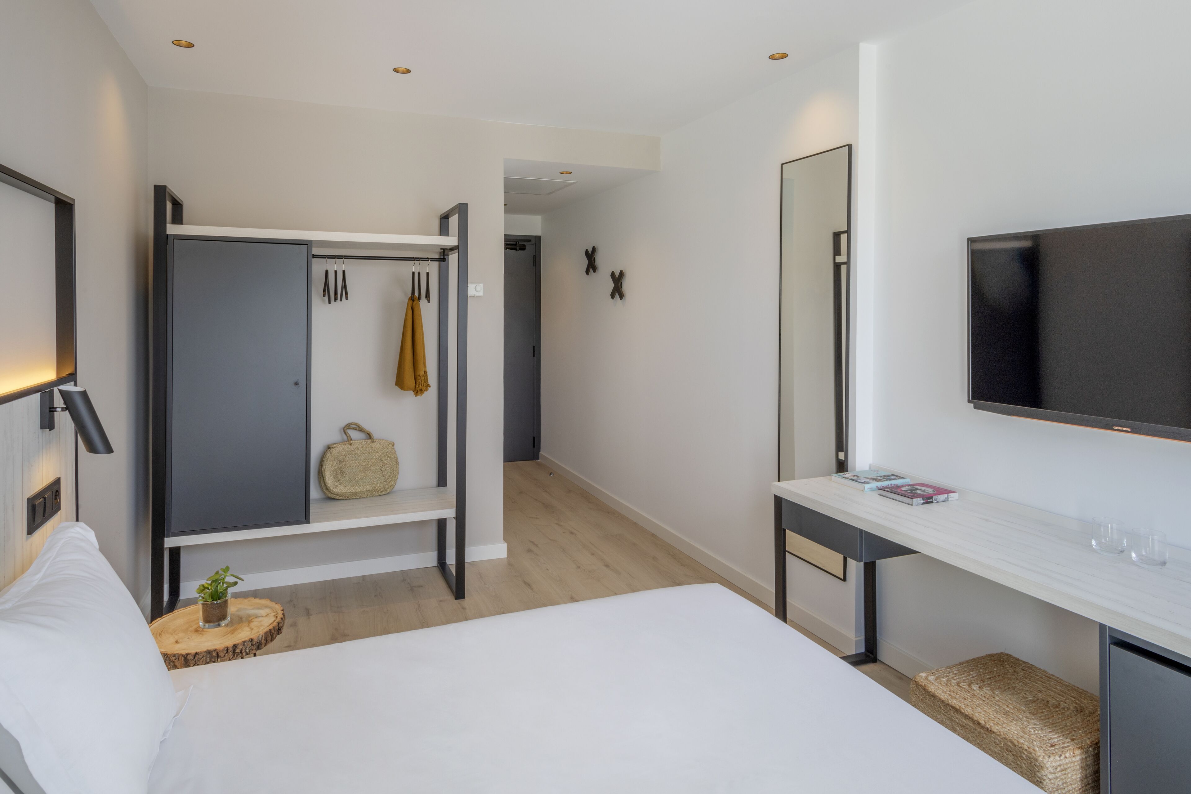 Habitación de hotel moderna con cama, escritorio con televisor de pantalla plana, armario y espejo.