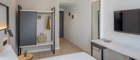 Habitación de hotel moderna con cama, escritorio con televisor de pantalla plana, armario y espejo.