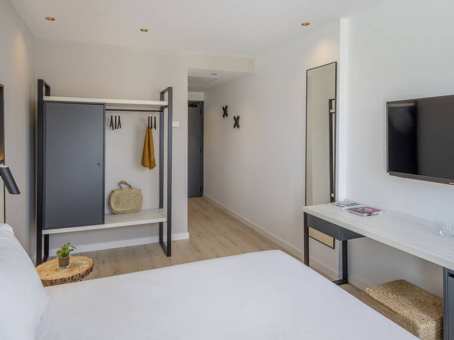 Habitación de hotel moderna con cama, escritorio con televisor de pantalla plana, armario y espejo.