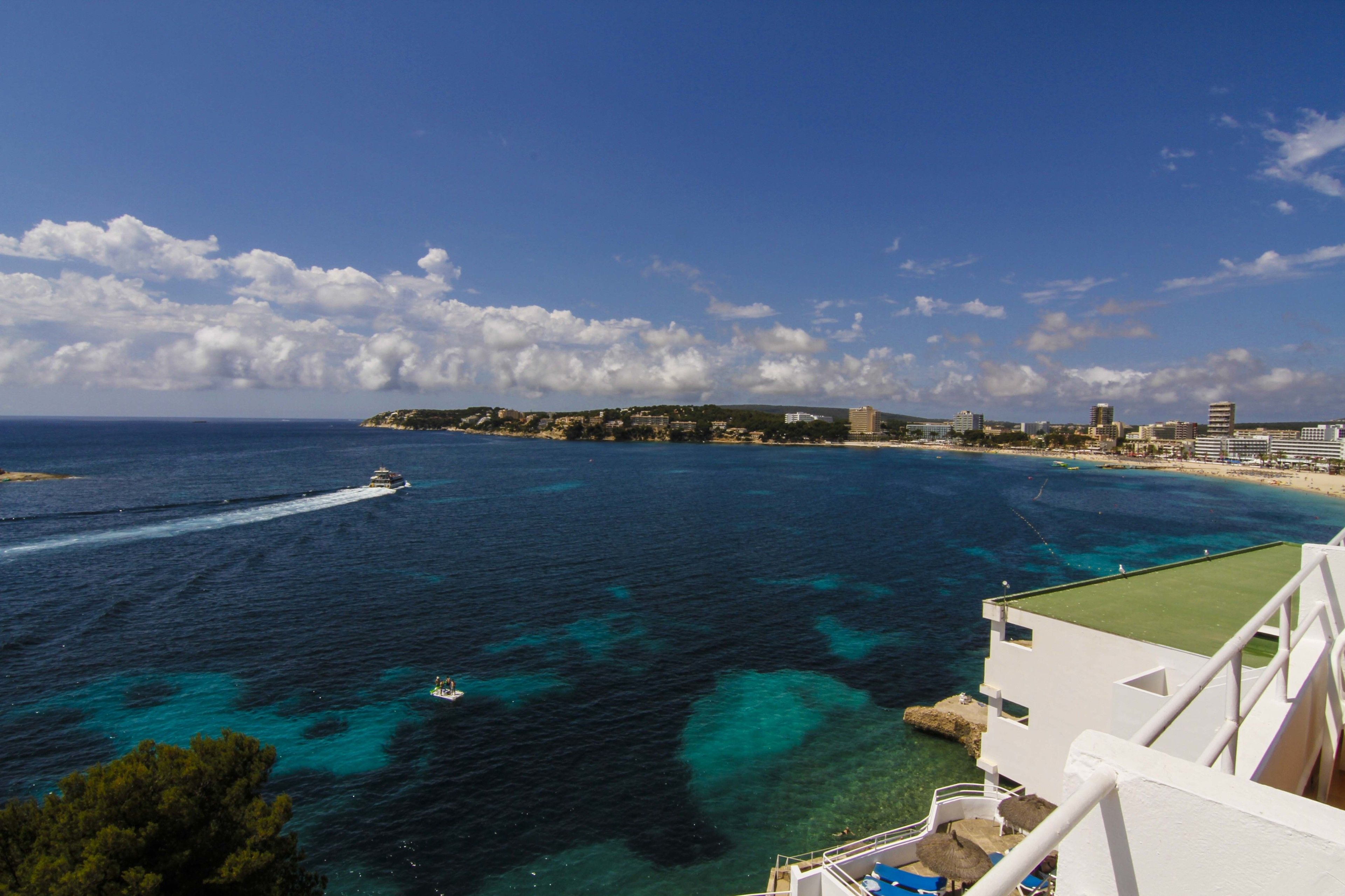 A coastal view with a boat on the water, a beach, and buildings in the distance.