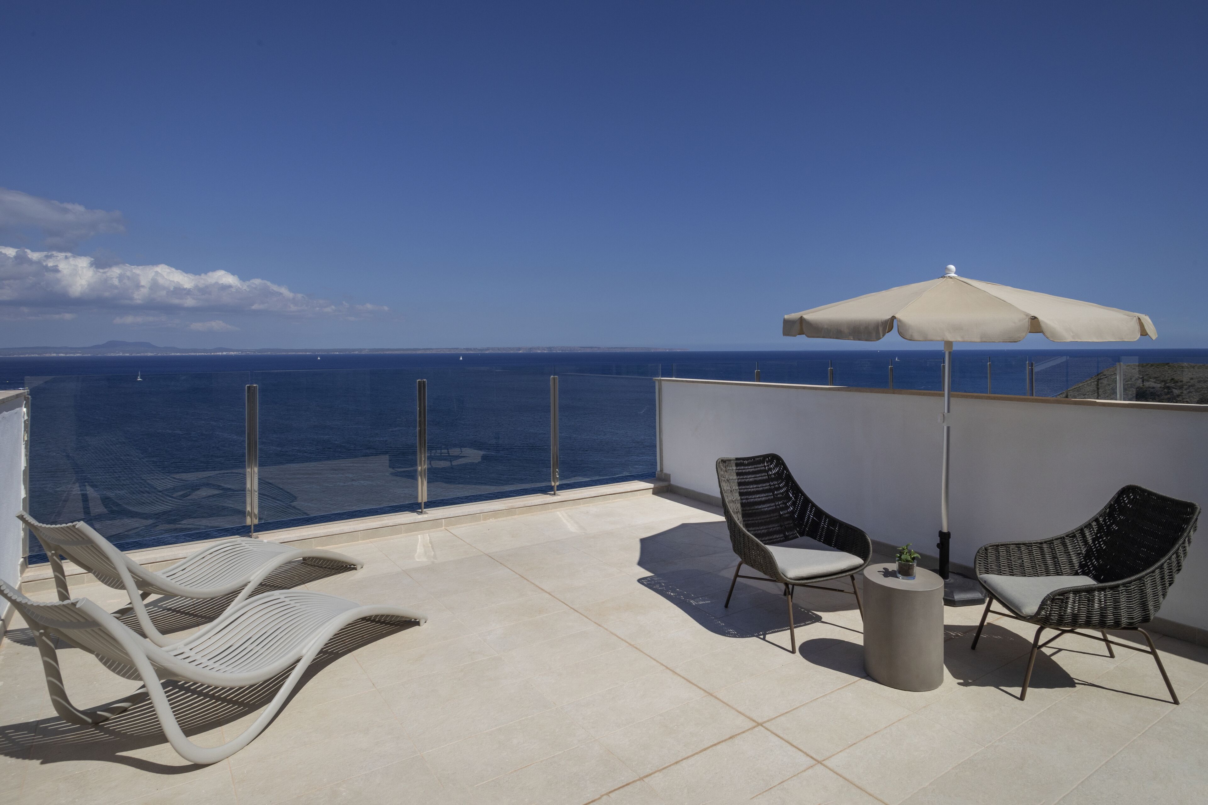 A balcony with two wicker chairs, a small round table, and a white umbrella.